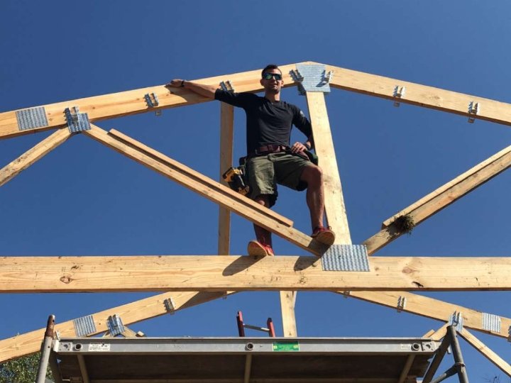 Lucas Redman standing on wooden roof trusses on a construction site