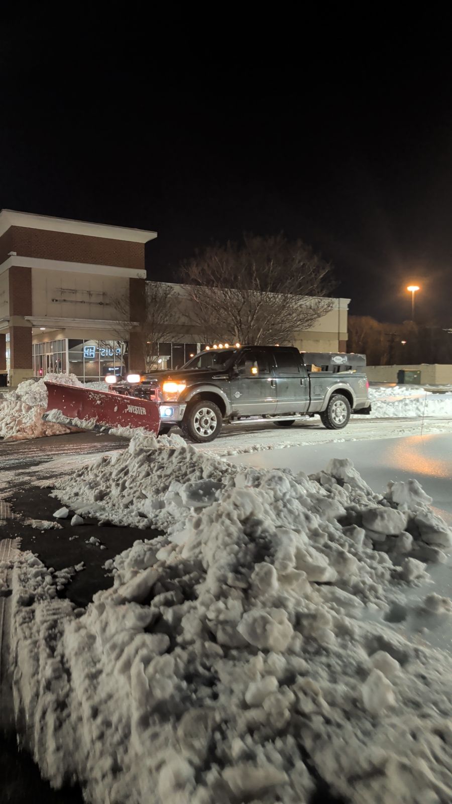 Pickup with snow plow clearing a lot at night